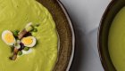 Gourmet green soup topped with bacon, quail eggs, peas, and plated in a ceramic bowl.