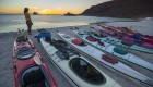 A row of kayaks on the beach while someone walks along the shore of the Sea of Cortez in Baja California Sur