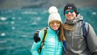 A couple smiles for a photo wearing sunglasses and beanies while on a winter trip through Patagonia 