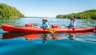 Two people in sun hats and sunglasses smiling in a red sea kayaking on a sunny day in British Columbia