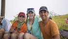 A man on the right and two women on the left smiling for a photo in a grassy field in the Galapagos on a foggy day