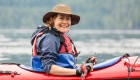 Woman in a sun hat and red life jacket in a red sea kayak smiling while holding her paddle across her kayak