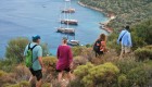 Four people walking across a ridge-line overlooking the sea full of yachts and boats in Turkey