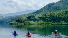 Three people kayaking on Lake Kivu surrounded my lush green rolling hills in rwanda