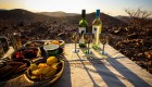 A table with three wine glasses, two bottles of wine, and a spread of chips and other light appetizers with the sunsetting behind it