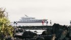 People walking across a bay of rocks along the beach with the Origin cruise ship in the background in the Galapagos Islands Archipelago