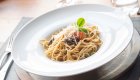 A white bowl of pasta on a nice place setting
