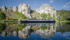 Classic French canal boat gliding past limestone cliffs and reflected on still waters, perfect for those Touring Sites in France.