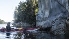 Sea kayaker paddling beside rocky coastal cliffs in British Columbia’s Johnstone Strait