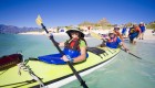 Two people in a green tandem kayak pushing off shore and into the crystal clear waters of the Sea of Cortez on a sunny day