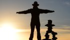 Traveler standing with arms outstretched at sunrise next to stone cairn in Peru – South America travel adventure