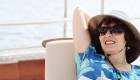 Women wearing sunglasses and a sun hat with her hands behind her head relaxing on a sun chair on a small yacht in Europe