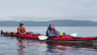 Two sea kayakers smiling while in calm waters off the shores of British Columbia.