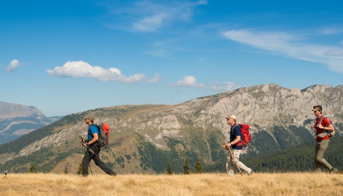 Three men hiking through across a grassy ridge line on a rocky landscape in Albania on a sunny day