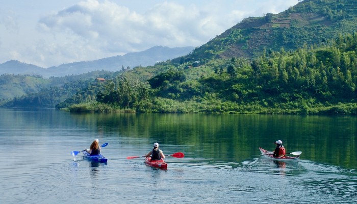 Three kayakers paddling on Lake Kivu surrounded by lush green hills in Rwanda, Africa